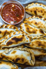 A box full of Argentine empanadas filled with meat. Along with a spicy sauce to go with it.