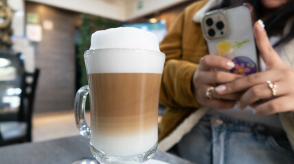 mano de mujer toma foto con su celular a taza de cafe con leche espumosa sobre mesa