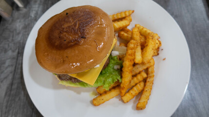 hamburguesa con queso amarillo, lechuga y papas a la francesa sobre plato blanco