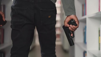 Policeman with gun walks along aisle in public library closeup. Security guy protects store with handgun. African American man prevents crime