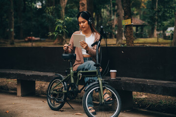 Happy young Asian woman while riding a bicycle in a city park. She smiled using the bicycle of...