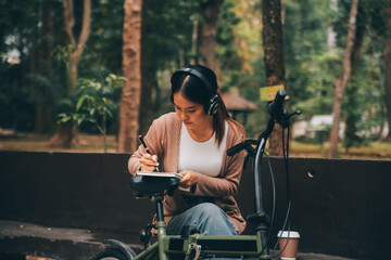 Happy young Asian woman while riding a bicycle in a city park. She smiled using the bicycle of...