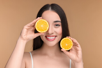 Beautiful young woman with pieces of orange on beige background