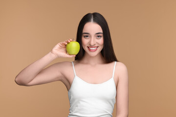 Beautiful young woman with apple on beige background