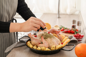 Woman cooking Chicken with orange and potato slices at wooden table, closeup