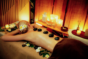 Hot stone massage at spa salon in luxury resort with warm candle light, blissful woman customer...