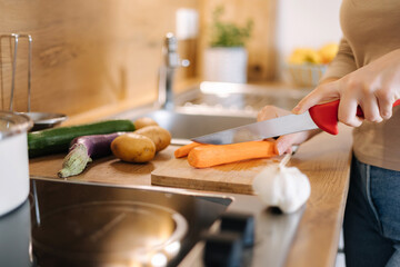 Close-up of female using knife and cutting carrot on wooden table. Home food concept 