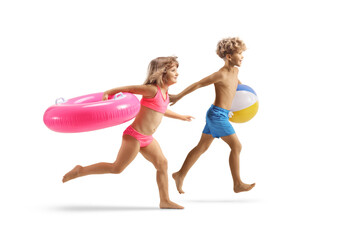 Obraz na płótnie Canvas Boy and girl in swimwear running and carrying a pink rubber swimming ring and a beach ball