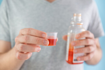 Man drinking dose of liquid medicine syrup for treatment cold and flu in measuring cup. Male taking liquid drug from meds bottle. Taking medicine, health care, pharmacy concept