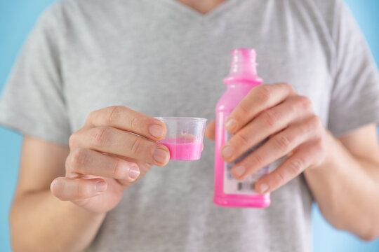 Man drinking antacid syrup to treat gastritis, stomach ulcer, heartburn, acid indigestion from measuring cup. Taking medicine, health care, pharmacy and treatment concept. Selective focus