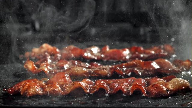 The bacon is fried in a pan with a splash of oil. Filmed on a high-speed camera at 1000 fps. High quality FullHD footage