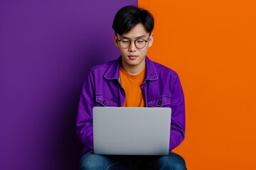 Focused Asian Man Working On Laptop Against Vibrant Purple Background: Perfectly Symmetrical And Captivating Photo With Ample Copy Space