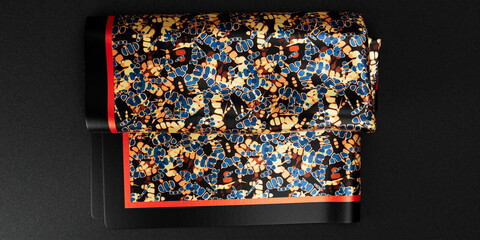 Abstract print silk pocket square with thick black and red border,  placed on top of a black  background. folded pocket square