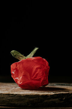 A red plastic bag sculpted to resemble a vegetable or fruit on a wooden surface against a black background