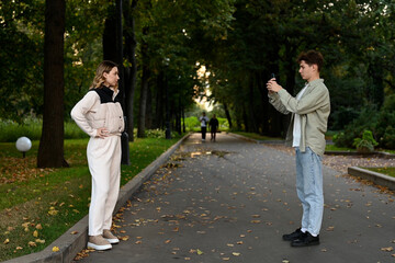 A guy takes a photo of his girlfriend on his phone in the park
