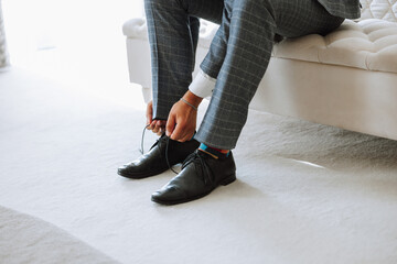 A young man put on black leather boots indoors. Close-up photo. Detail of a groom putting on his...