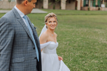 A handsome groom and an elegant bride in a lush white dress are walking in a summer park. Happy bride and groom getting ready for their best day.