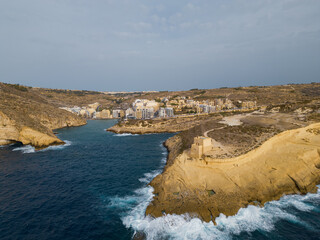 Aerial view of Xlendi tower and Xlendi town on Gozo island with scenic waves hitting the rock.