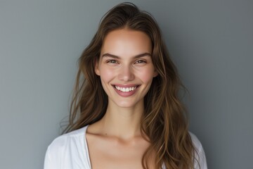 Fototapeta premium Stunning Supermodel Poses With Natural Makeup, Radiant Smile, Against Grey Studio Backdrop: Perfectly Symmetrical Photo With Copy Space