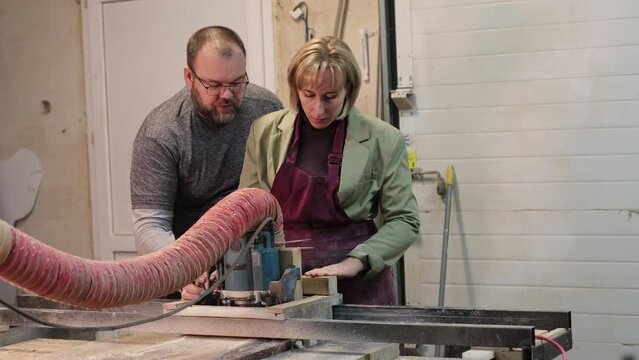 A man instructs a woman at a saw machine. This scene emphasizes gender diversity in trade skills and the mentorship trend.