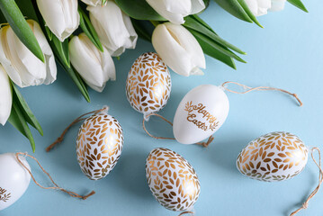 Floral border from bouquet of white tulips, Easter eggs and toys on blue background. Easter celebration concept. Copy space. Top view