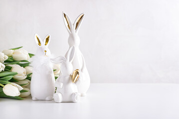 Three Easter rabbits figurines with bouquet of white tulips on white background. Easter celebration concept. Copy space. Front view - obrazy, fototapety, plakaty