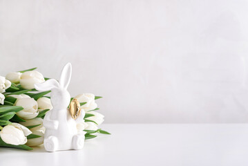 Easter rabbit figurine with bouquet of white tulips on white background. Easter celebration concept. Copy space. Front view