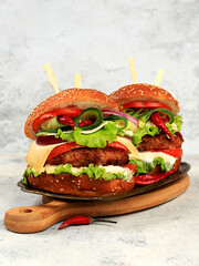 Two double cheeseburgers with fresh lettuce, tomato, cream cheese, cucumber, onion, chili pepper and cutlet on an old wooden board, food delivery concept, menu and advertising for cafe