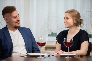 A girl and a boy talk over a glass of wine.