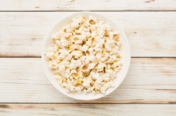 Bowl with popcorn on wooden background, top view