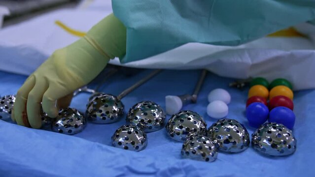 Acetabular reamer of stainless steel on the surgical stand. Doctor takes one of the items. Close up. Orthopedic equipment and materials in surgery room.