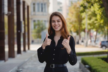 Young happy pretty smiling professional business woman, happy confident positive female entrepreneur standing outdoor on street thumbs up, looking at camera, 