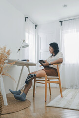 Woman with prosthetic leg sitting in chair in living room at home. Relaxed, happy woman at home living room sitting on the chair, using tablet