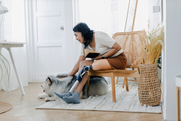 Woman with prosthetic leg sitting in chair near dog in at home. Woman sitting on chair with dog at...