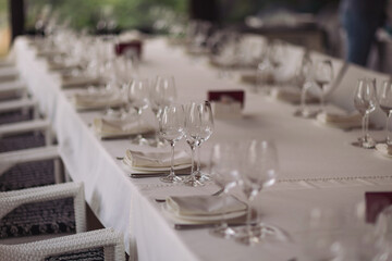 Table setting for a party or wedding reception in a restaurant. Row of ladder-back chairs set around elegant dining table with white tablecloth and crystal glasses. 
