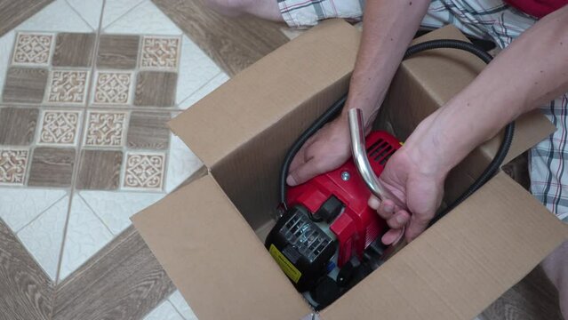 a man pulls a brush cutter out of the box, new brushcutter, unpacking garden equipment from the box, garden equipment for mowing grass