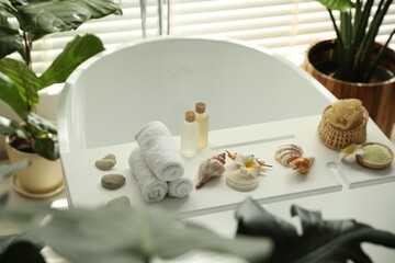 Bath tray with spa products, towels and shells on tub in bathroom