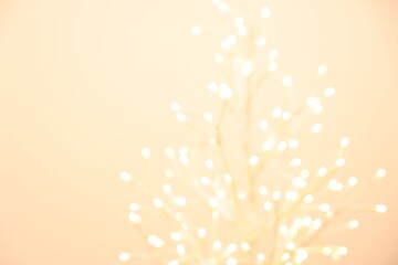 Decorative tree with lights on beige background, blurred view. Space for text