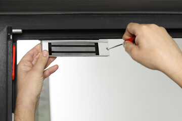Man with screwdriver installing electromagnetic door lock indoors, closeup. Home security