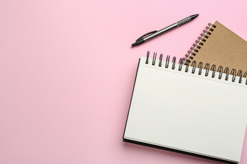 Notebooks and pen on pink background, top view. Space for text