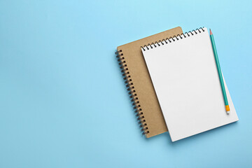 Notebooks and pencil on light blue background, top view. Space for text