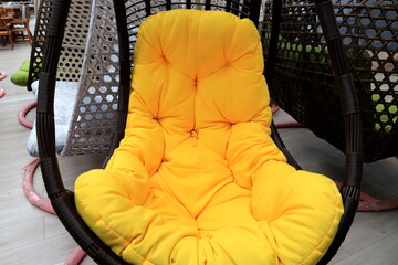 Rattan cocoon chair, garden furniture with yellow cushion in store. Beautiful fashionable modern...