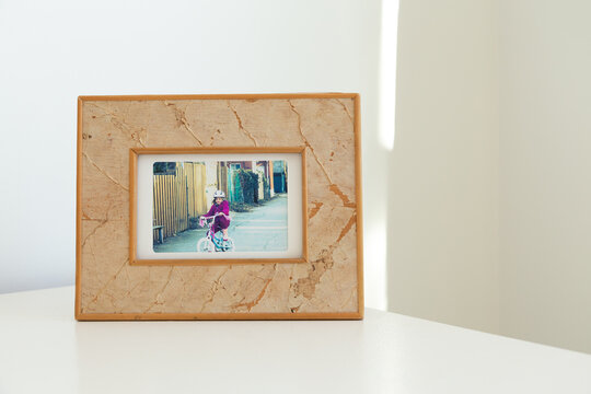 Selective focus view of framed portrait of little girl on a bicycle set on pale cream table in natural light