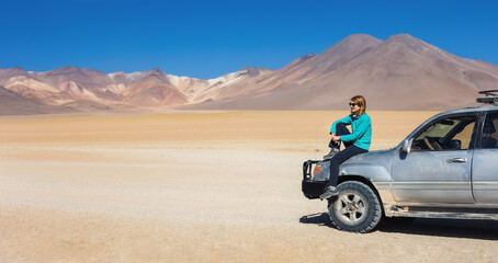 A girl tourist sits on a car in the desert of Salvador Dali. Bolivia