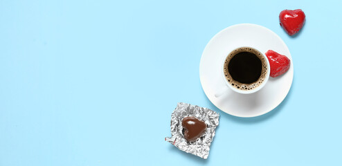 Cup of coffee with heart-shaped chocolate candies on blue background with space for text....