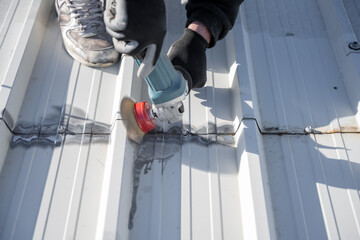 Man removing rust from white metal roof with grinding tool. Man holding grinder. Roof maintenance....