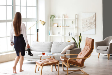 Young businesswoman with taken shoes at home after long working day