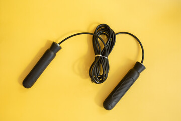 Skipping rope with black handles on the yellow background. 