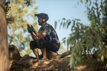 Male mountain cyclist checking his phone sitting on a rock with his bike by his side
