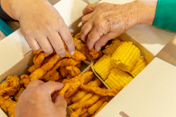 closeup of three hands taking food from a fast food box with chicken, corn, french fries and arepas in a food court